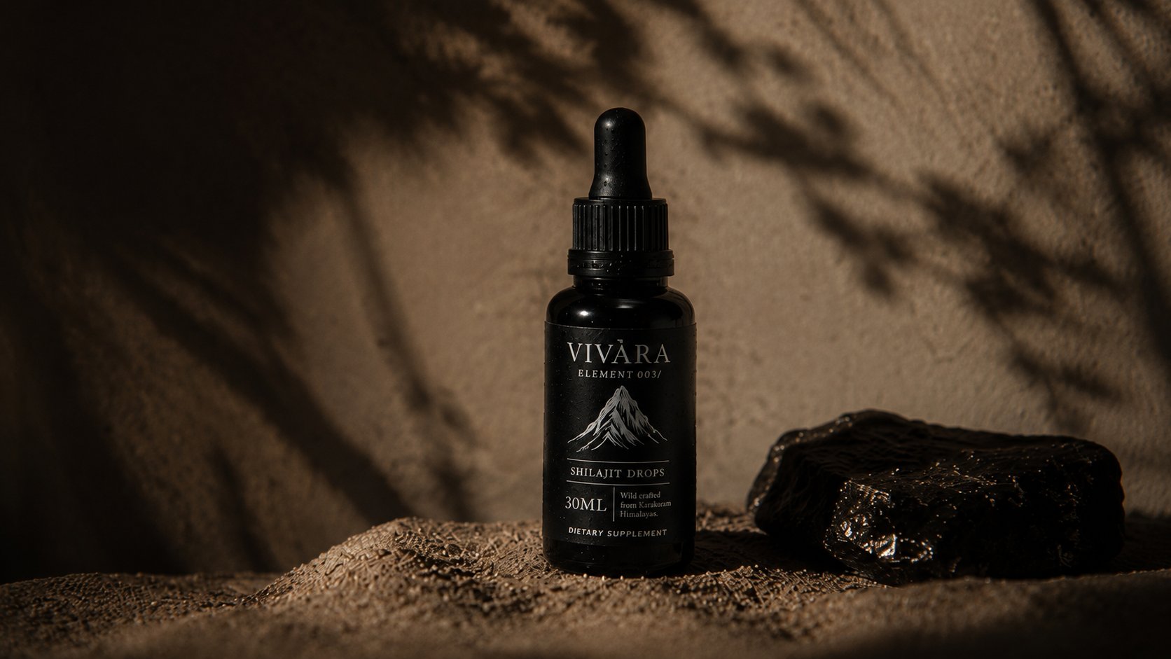 Element 003 resting on fine sand beside raw shilajit resin